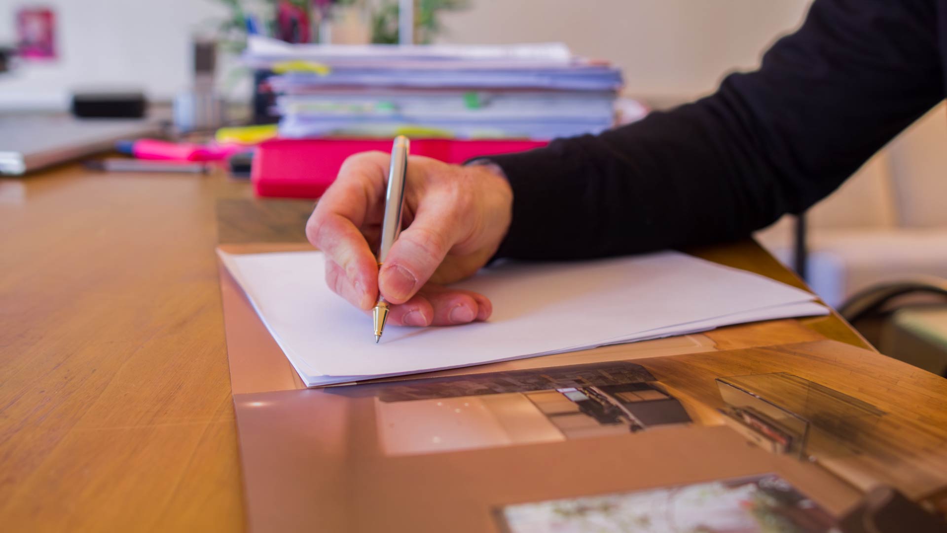 Le geste derrière chaque stratégie Main d’un avocat écrivant sur une feuille, avec des dossiers et brochures en arrière-plan